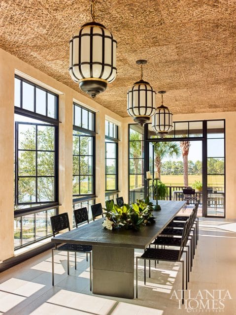 Dining room with a textured ceiling, large windows overlooking water and greenery, a long dark wood table with black chairs, and ornate pendant lights.
