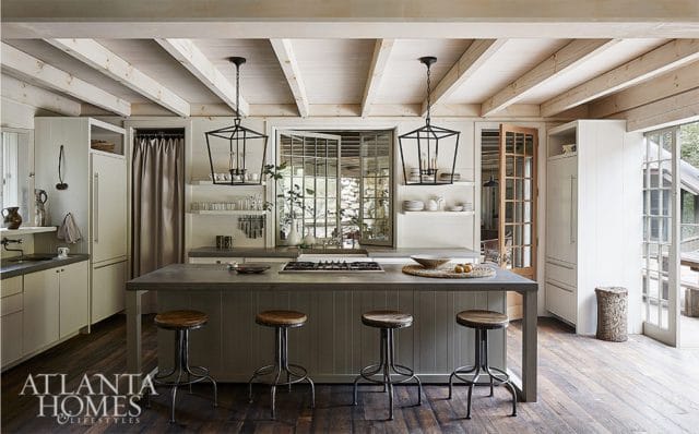 Kitchen with gray island, wooden stools, white cabinetry, and exposed wooden beams on the ceiling. Two black lantern pendant lights hang above the island.