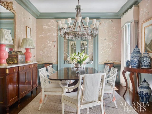 Dining room with a dark wood table and chairs, chinoiserie wallpaper, a crystal chandelier, and blue and white ginger jars on a console table.