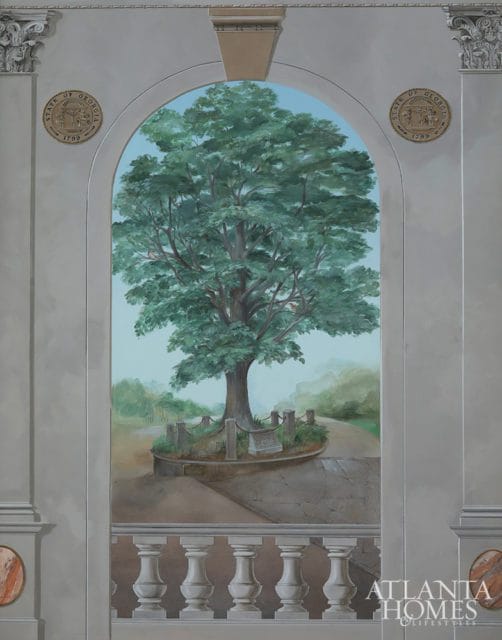 Mural depicting a large tree in a park setting, framed by an archway with classical columns and balustrades. The State of Georgia seal appears on either side of the arch.
