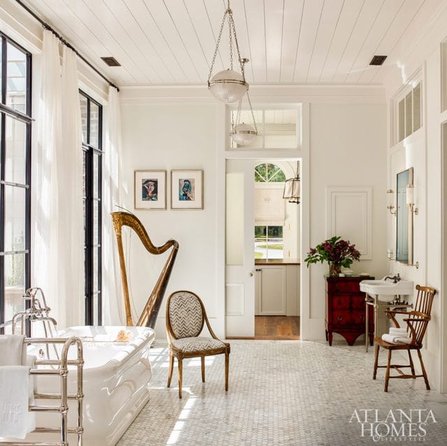 Bright bathroom with white hexagonal tile floor, freestanding tub, harp, patterned chair, and red dresser with sink.
