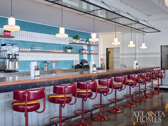Bar with red leather stools and a long wooden counter, backed by a wall with blue and white tile and shelves.