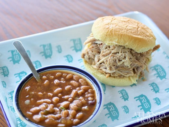 Pulled pork sandwich and baked beans served on a white tray with blue trim and patterned paper