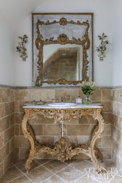 Bathroom with a marble-topped vanity featuring ornate carved wood legs, a white sink, and a large antique mirror with a gold frame.