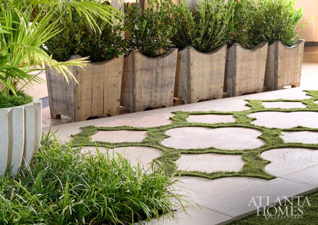 Row of weathered wooden planters filled with greenery, next to a pathway of light-colored pavers interspersed with mossy ground cover.