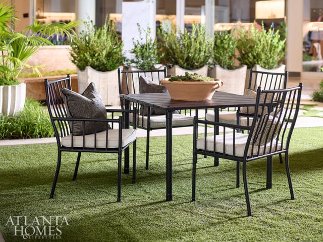 Black metal outdoor dining set with cushioned seats and decorative pillows on artificial turf, surrounded by potted plants.