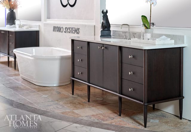 Dark wood vanity with white marble countertop and silver hardware, freestanding white bathtub, and patterned tile flooring.