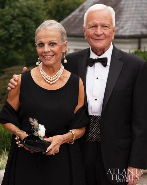Elderly couple in formal wear, woman wears pearls and black dress, man wears tuxedo.
