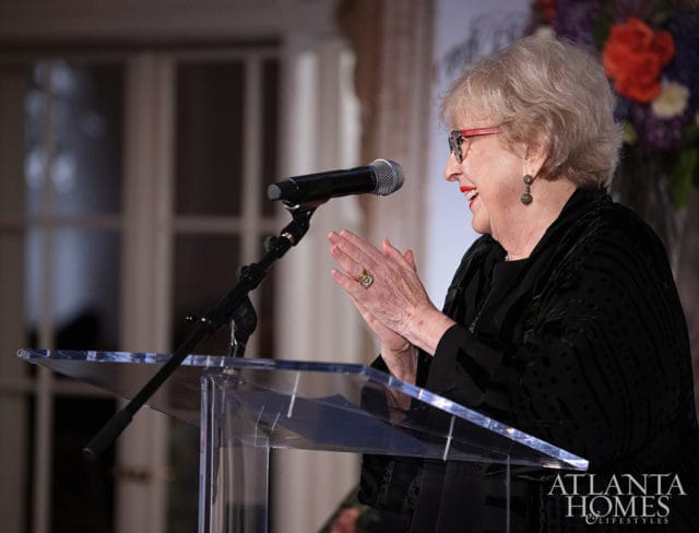 Woman in black speaking at a podium, clapping her hands.