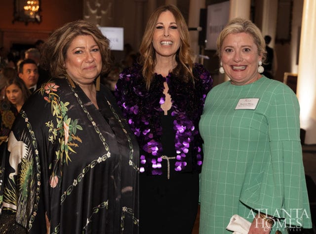 Three women smiling, one in a black floral robe, one in a purple sequined jacket, one in a green