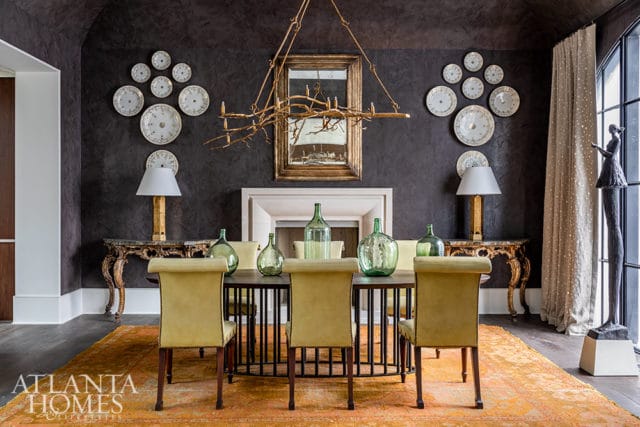 Dining room with dark walls, yellow chairs, and an orange rug. Features a fireplace and decorative