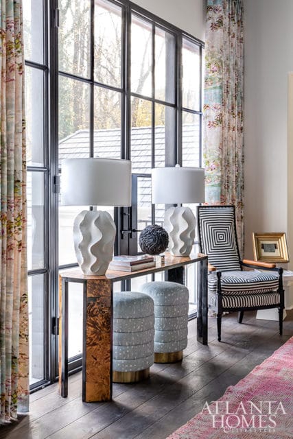 Console table with wavy white lamps, patterned chair, and floral curtains