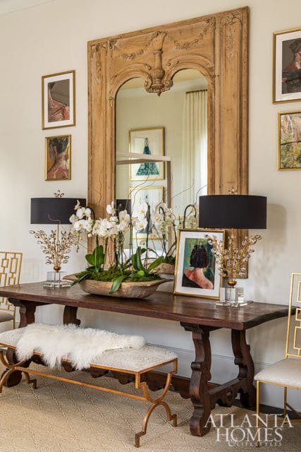 Entryway with dark wood console table, white orchids, black lamps, and ornate mirror.