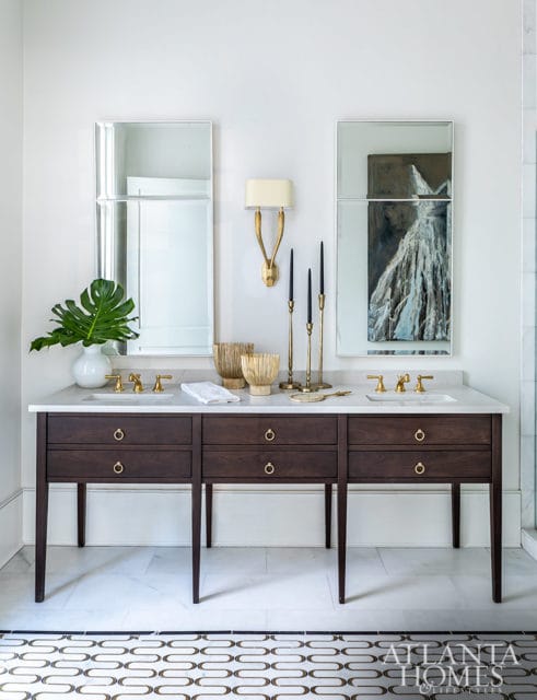 Double vanity with dark wood drawers, marble countertop, brass fixtures, and two mirrors.