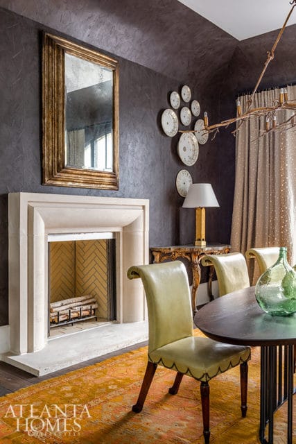 Dining room with stone fireplace, gold mirror, leather chairs, and patterned rug.