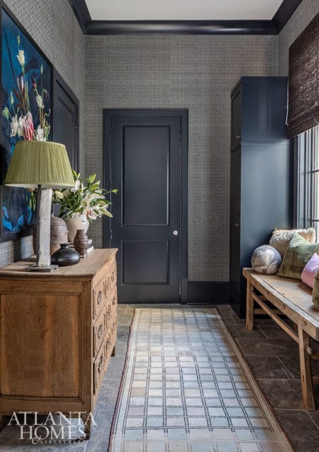 Hallway with gray patterned wallpaper, dark gray door, wooden dresser, and bench.