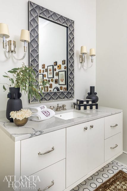 White vanity with marble countertop, geometric mirror, and sconces.