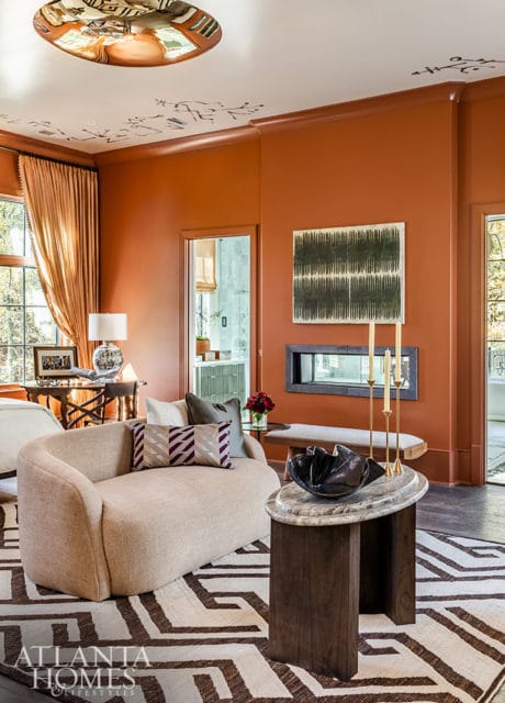 Living room with rust-colored walls, a curved beige sofa, geometric rug, and modern fireplace.