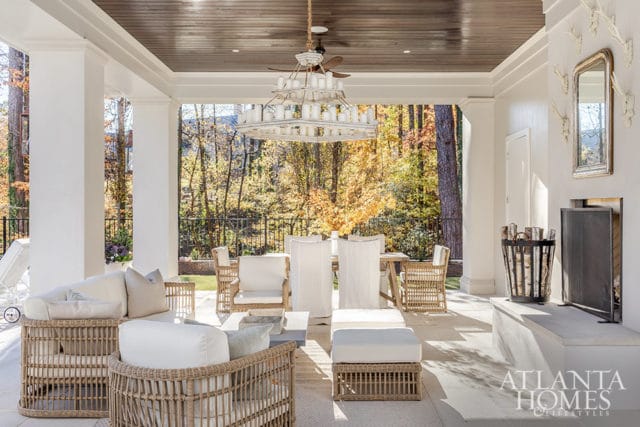 Covered patio with wicker furniture, dining set, fireplace, and autumn foliage view.