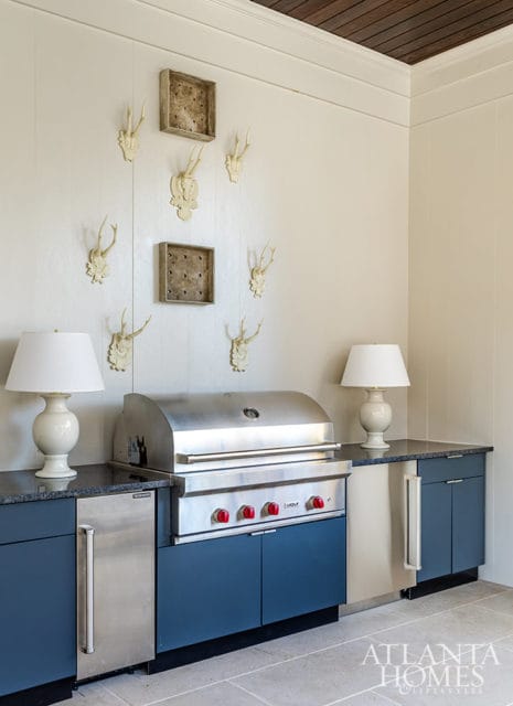 Outdoor kitchen with stainless steel grill, navy cabinets, and wall decor of antlers