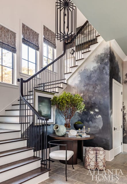 Foyer with a grand staircase, abstract tree mural, round table with decor, and a black geometric