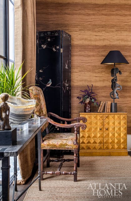 Wooden paneled wall, black folding screen with birds, ornate chair, and yellow cabinet with lamp