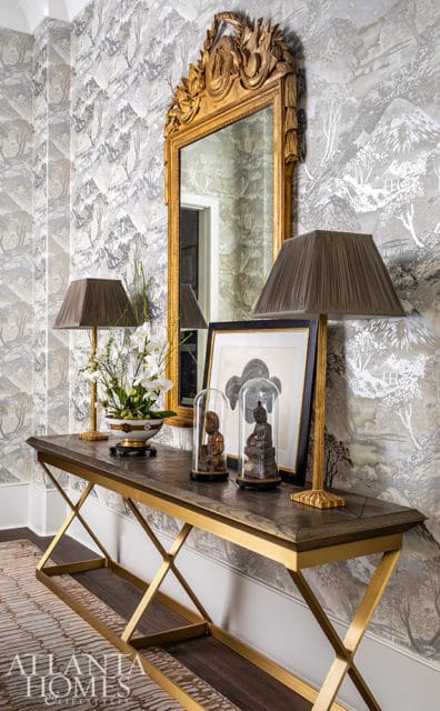 Console table with gold frame and wood top, topped with lamps, floral arrangement, and decorative