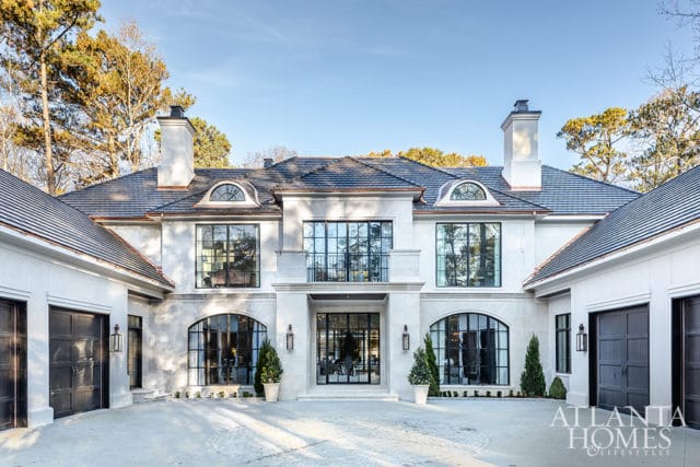 Modern white stone house with dark metal-framed windows and doors, arched garage doors, and