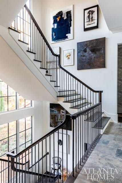 Staircase with dark wood banister and black spindles, white walls adorned with abstract art.