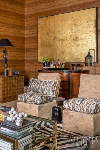 Living room with wood-paneled walls, gold abstract art, and cork chairs with patterned pillows.