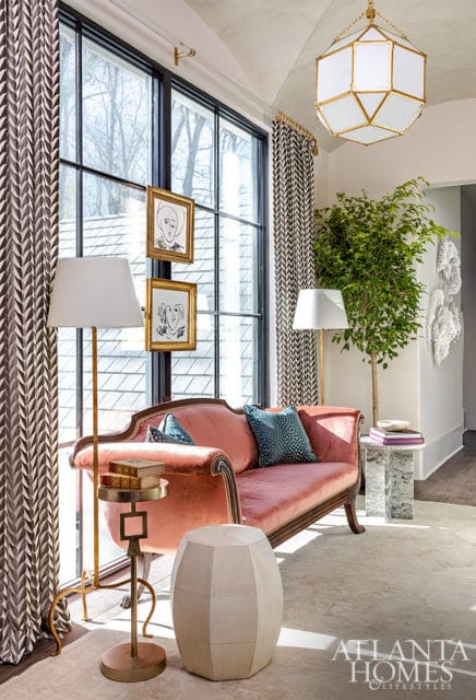 Pink velvet sofa with patterned pillows, brass floor lamps, and geometric stool.