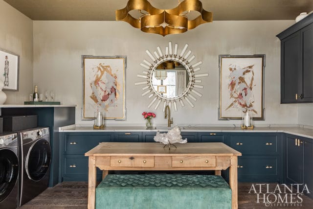 Laundry room with dark blue cabinets, marble counters, abstract art, and sunburst mirror.
