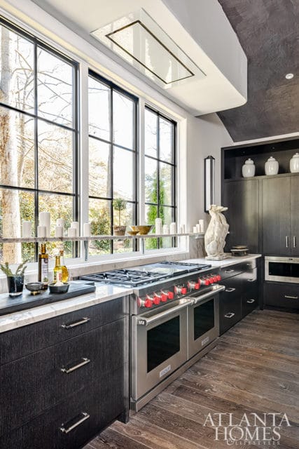 Dark wood kitchen with stainless steel range, marble countertops, and large windows.