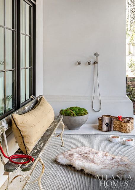 Outdoor shower with dog bowls, baskets, and a moss-filled planter on a rug.