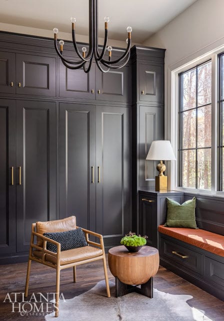Dark gray built-in cabinets with brass hardware, leather armchair, and window seat.