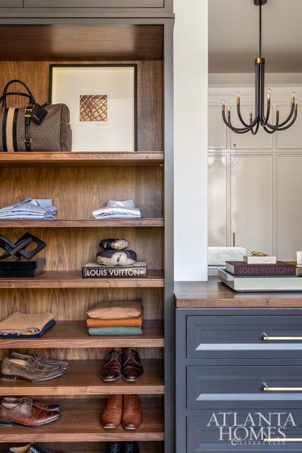 Closet with wood shelves holding clothing, shoes, and Louis Vuitton books. Dark gray drawers below.