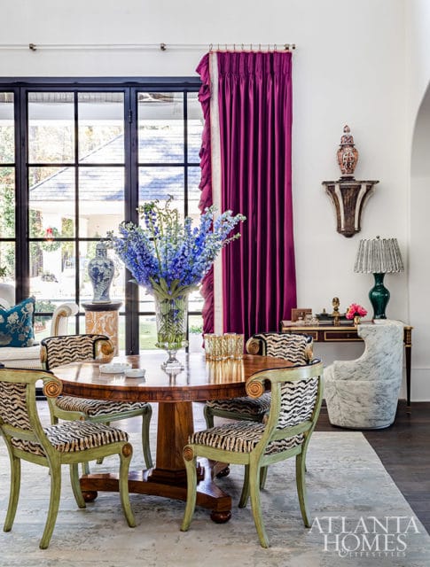 Dining room with round wood table, zebra print chairs, and purple curtains.
