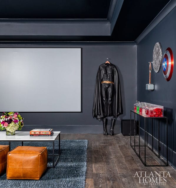 Dark gray room with a projector screen, Batman costume, Captain America shield, and Thor's hammer.