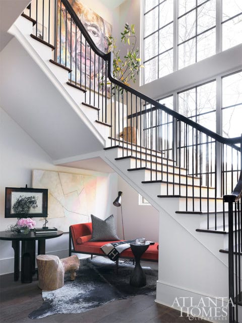 Staircase with black railings, abstract art, red chaise lounge, and cowhide rug.