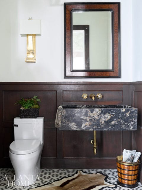 Powder room with white toilet, black granite sink, brass fixtures, and wood paneled walls.