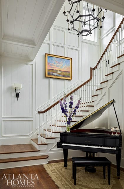 Grand piano in entryway with white paneled walls and staircase