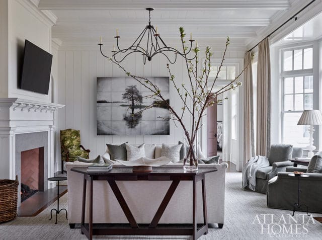 Living room with white paneled walls, fireplace, sofa, and artwork of a tree in water.