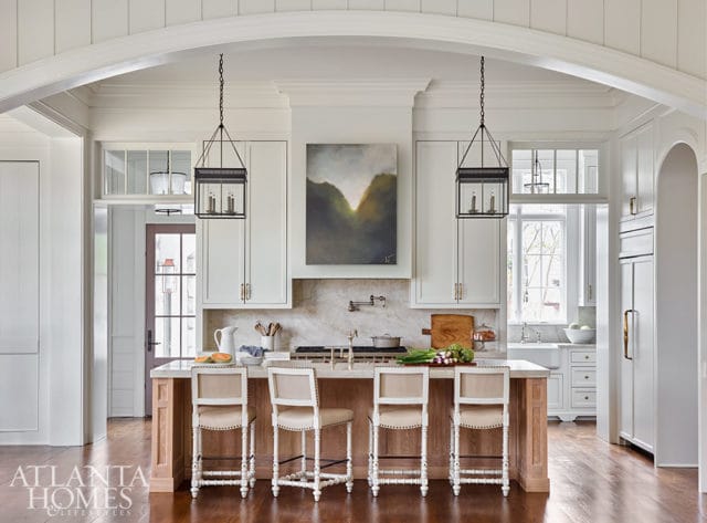 White kitchen with marble backsplash, island with wood base, and four upholstered bar stools.