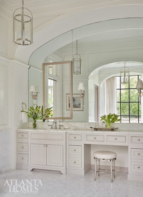 White bathroom with marble countertops, light gray cabinetry, and a vanity stool.
