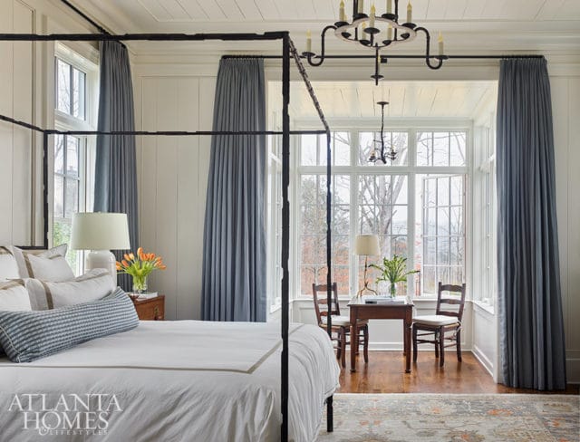 Bedroom with four-poster bed, blue curtains, and bay window overlooking trees.
