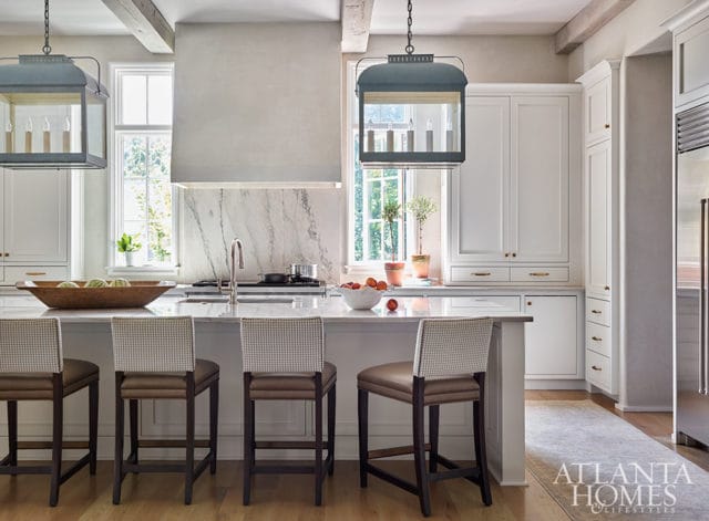 White kitchen with marble backsplash, island with bar stools, and pendant lights.