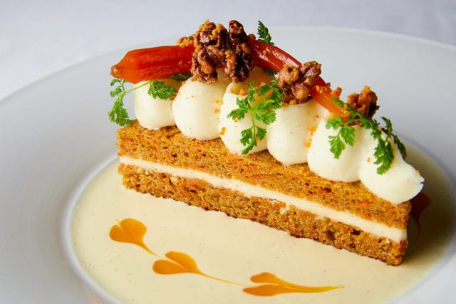 Carrot cake slice with cream cheese frosting, candied walnuts, and apricot.