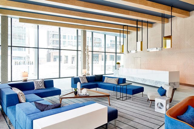 Lobby with blue sectional sofas, geometric patterned wallpaper, and a white reception desk.