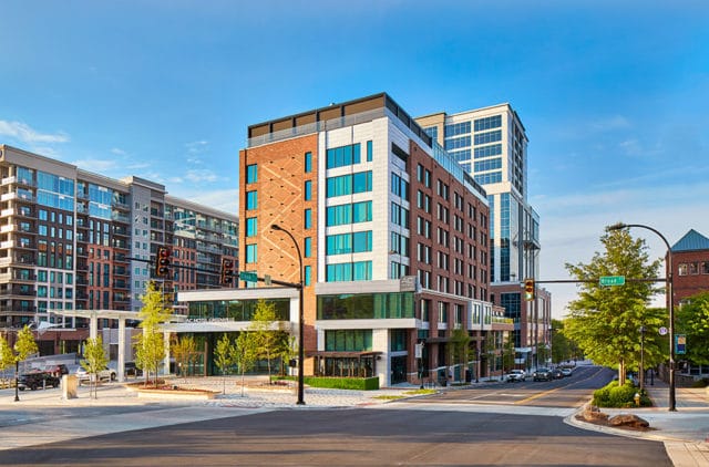 AC Hotel Greenville with brick and white facade, glass windows, and surrounding cityscape.