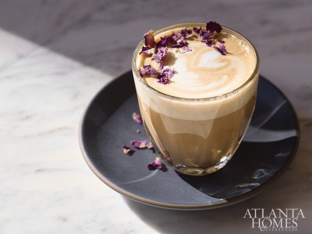 Latte with foamed milk and dried rose petals on a dark plate.